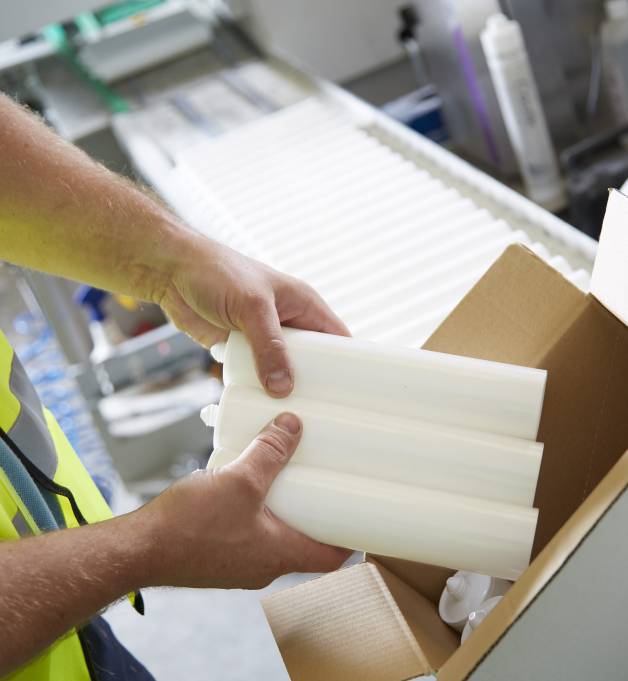 A factory worker packing three unbranded silicone tubes into a box.